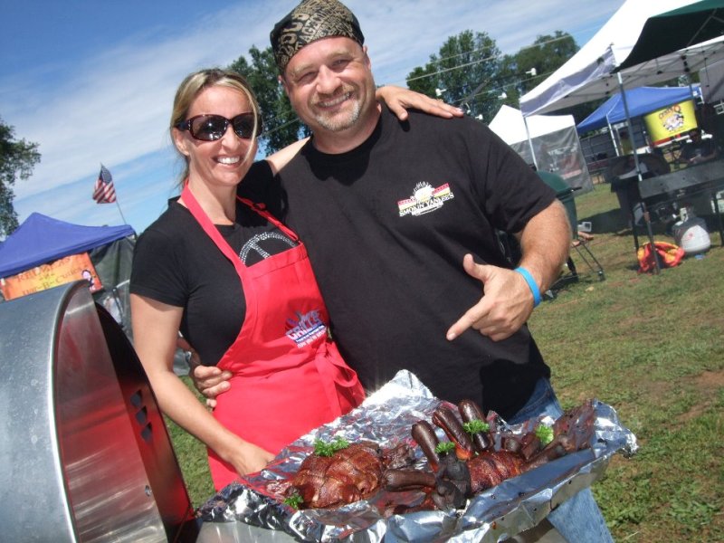 Bekah and Chris Juencke wearing Smokin' Yankee apron and t-shirt point at barbequed meat